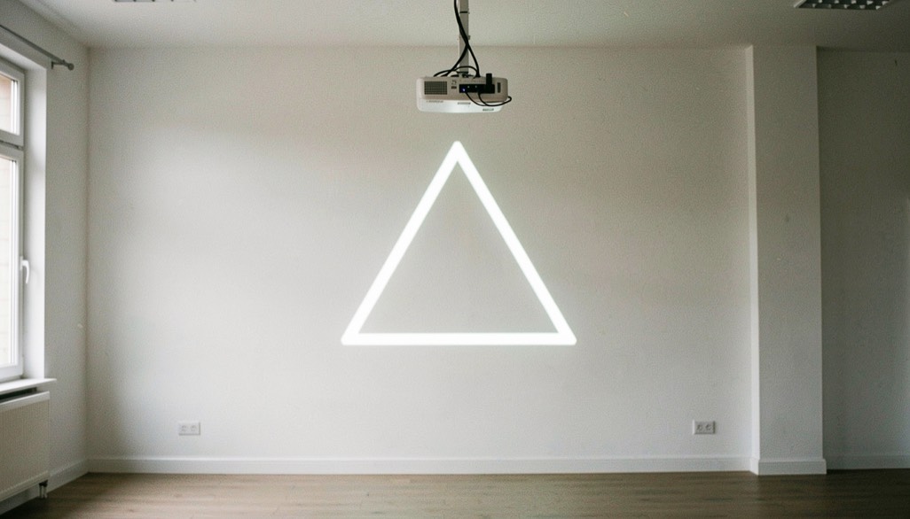 Vidéoprojecteur fixé au plafond projetant un triangle lumineux sur le mur blanc d’une pièce vide